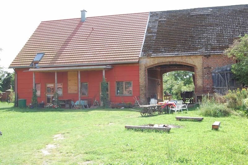 Rotes Wohnhaus neben der alten Scheune mit Backsteinbogen, davor eine Wiese mit Feuerstelle und Sitzgelegenheiten