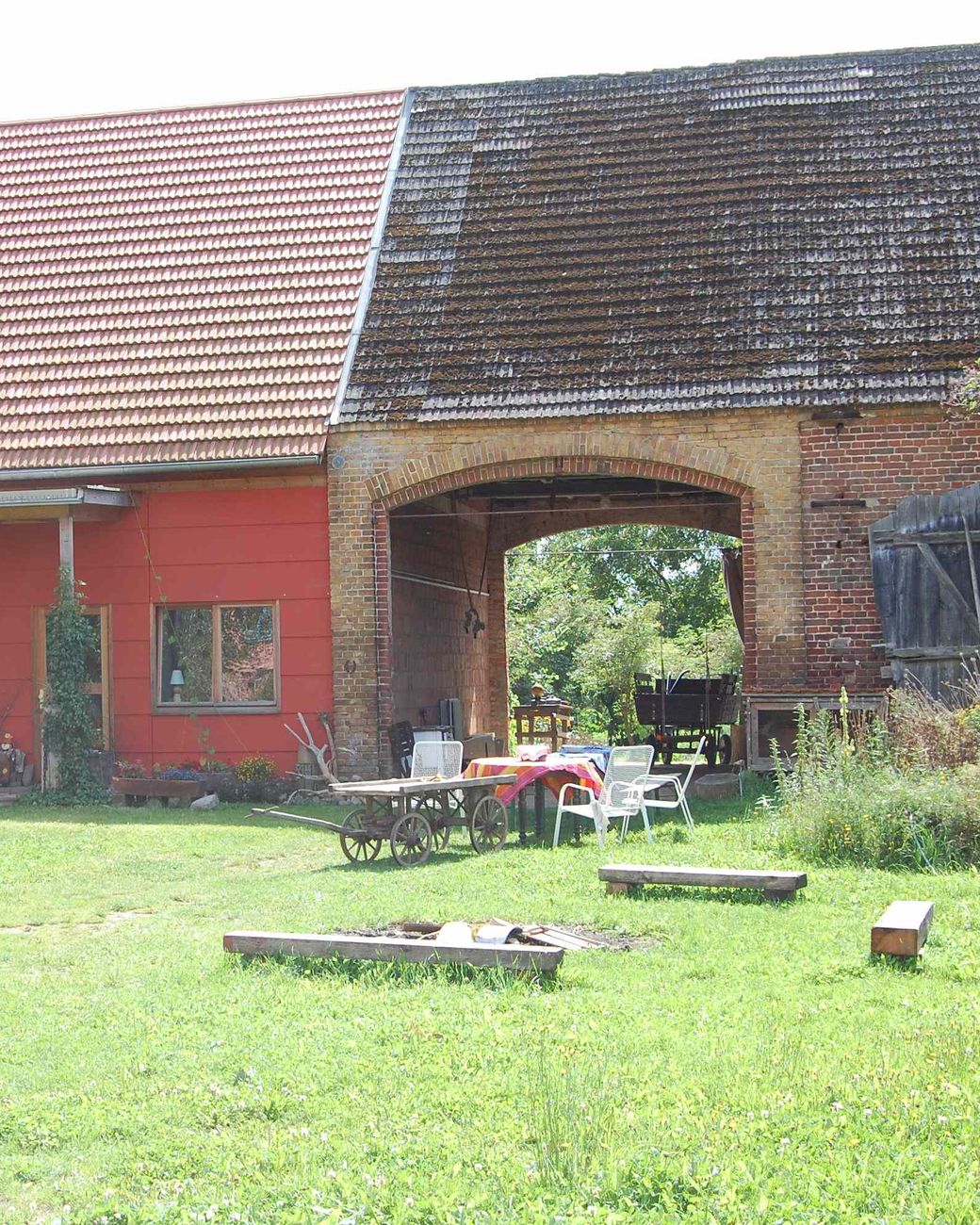 Backsteinbogen der alten Scheune, daneben die rote Wand des Wohnhauses